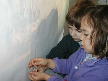 Figures 9-11. A child assists her peer in tracing shadows in preparation to paint.